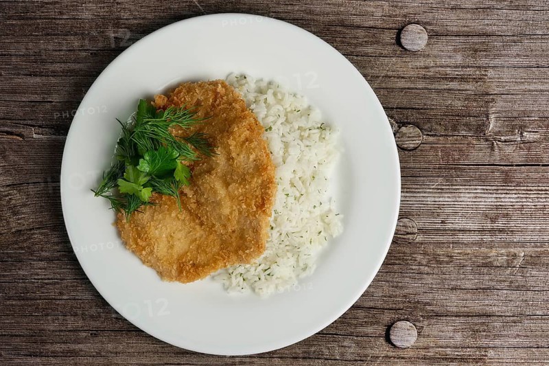 Top view of chicken fillet in breading with rice on wooden table