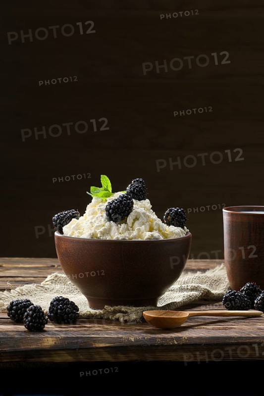Dairy product cottage cheese and milk in brown ceramic bowl with spoon on wooden table