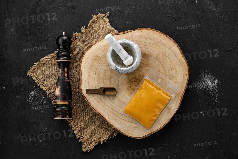 Wooden cross section with turmeric in plastic package and stone mortar and mill
