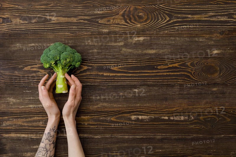 Overhead view of fresh broccoli in hands over wooden background