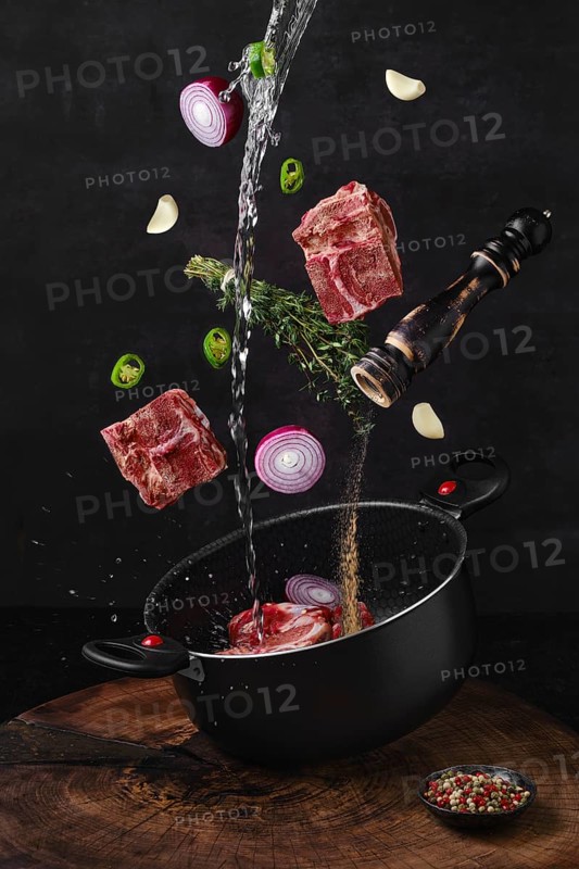 Chopped beef bones falling into saucepan with ingredients for bouillon stock