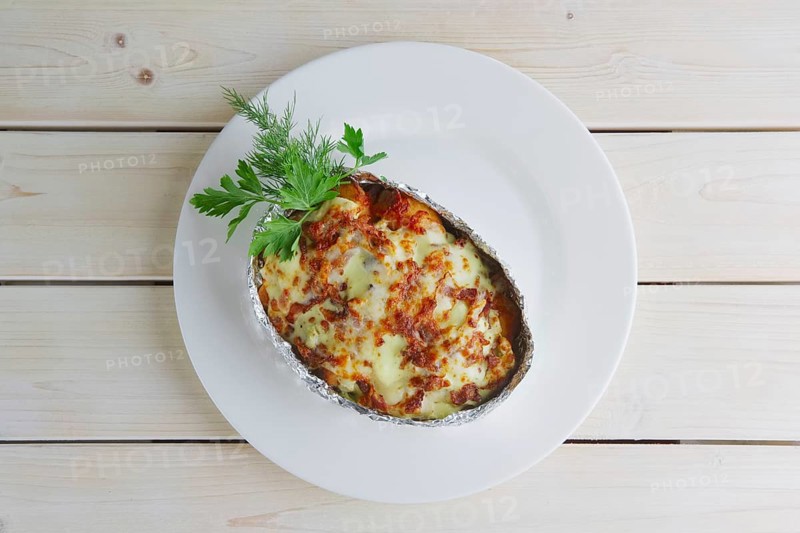 Top view of meat baked in foil with vegetables and cheese on wooden table