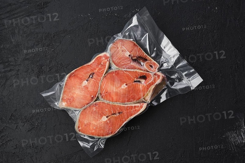 Overhead view of raw salmon steak in vacuum packaging on dark background