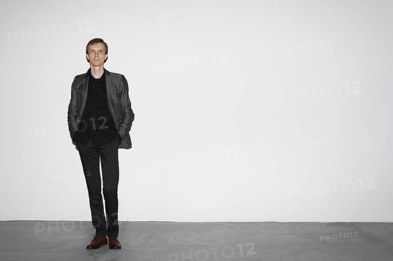 Man in wool jacket standing near white concrete wall with hands in pocket