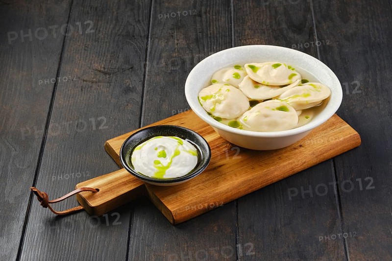 Bowl with beef pelmeni with sour cream on a wooden serving board