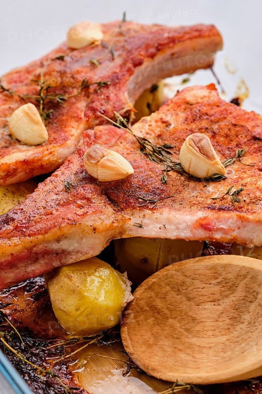 Steak with bone and potato baked in oven in a roasting pan with garlic and thyme