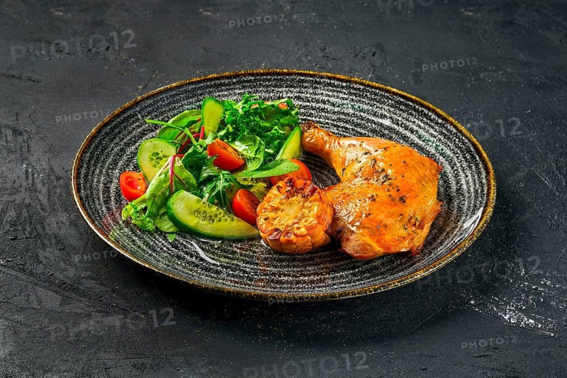 Baked chicken thigh served with fresh vegetables and grilled corn on dark background