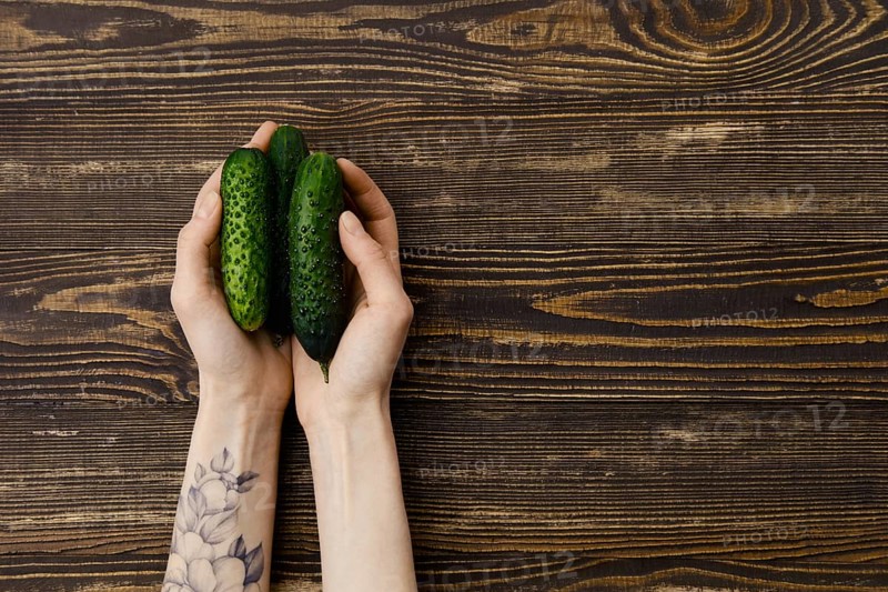 Overhead view of fresh cucumbers in hands over wooden background