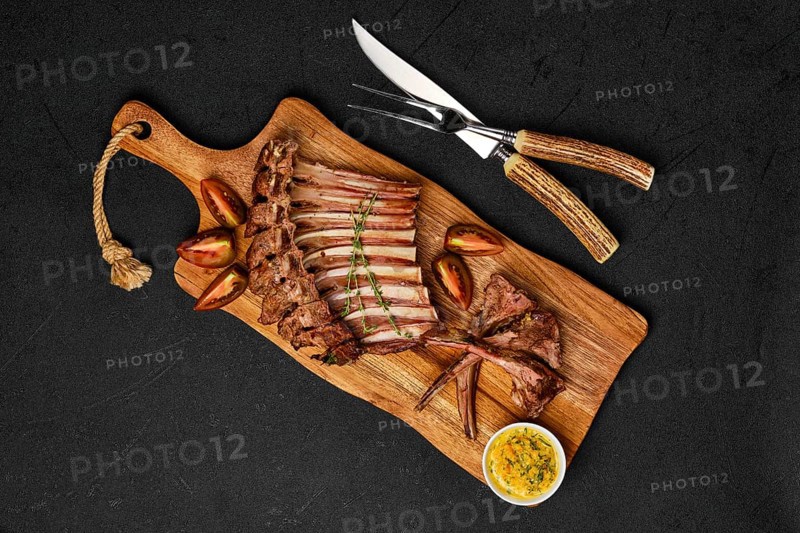 Overhead view of grilled ribs of lamb on a plate with spicy sauce