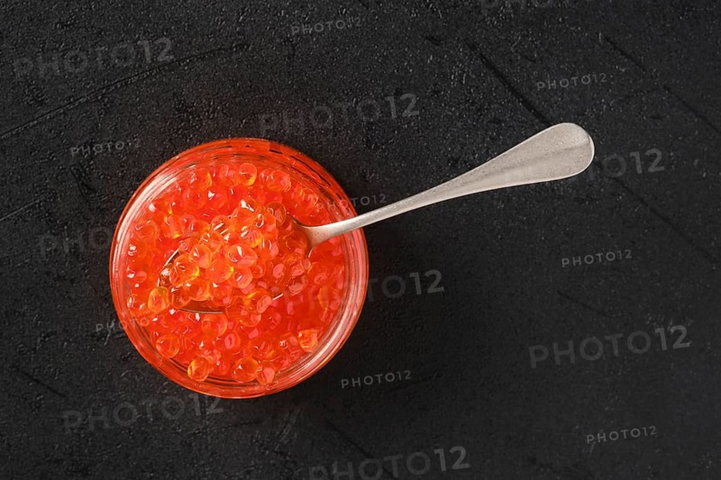 Overhead view of open jar with red caviar and a spoon in it
