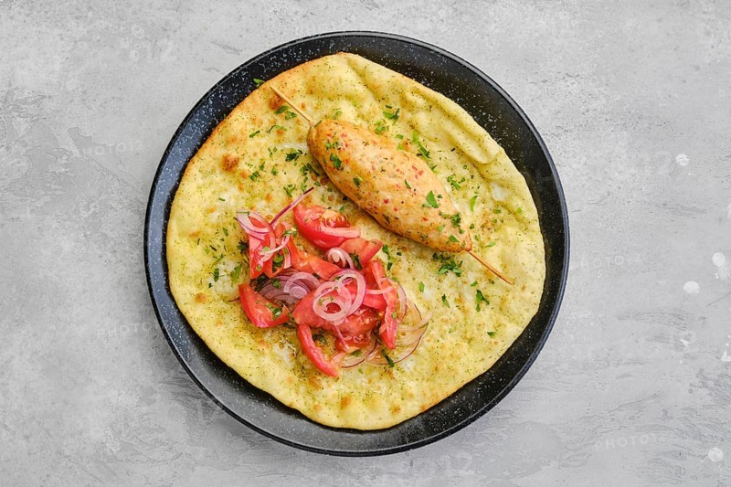 Top view of kebab served on tortilla with tomato and red onion