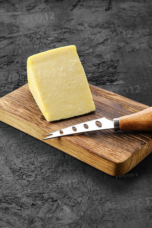 Triangular piece of hard cheese on wooden cutting board