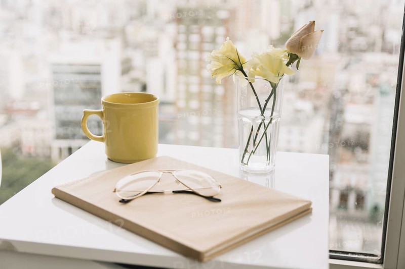 Glasses book near flowers mug table