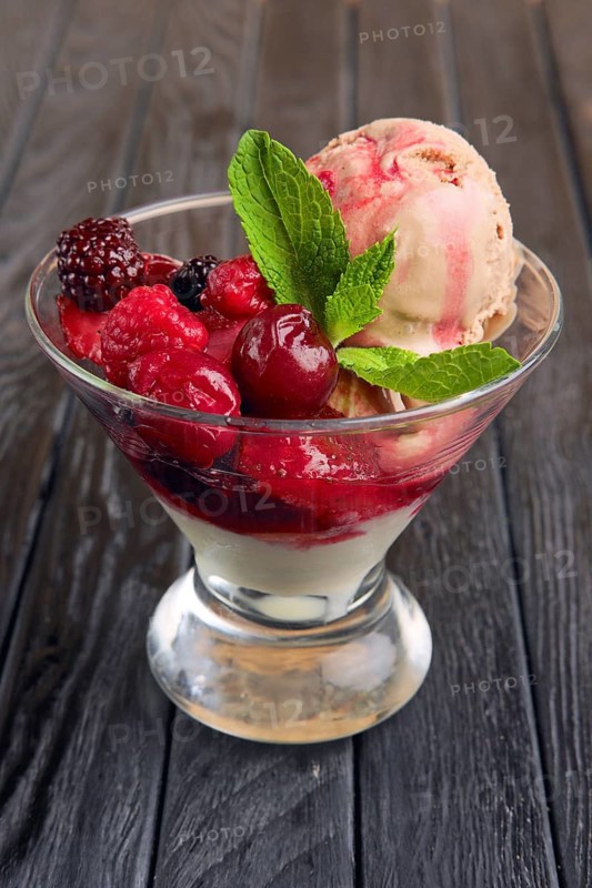 A cup of cherry ice cream decorated with raspberries and dewberry and mint leaves