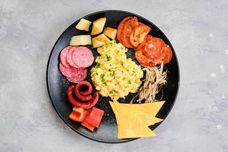 Top view of a plate with scrambled eggs with various sausages
