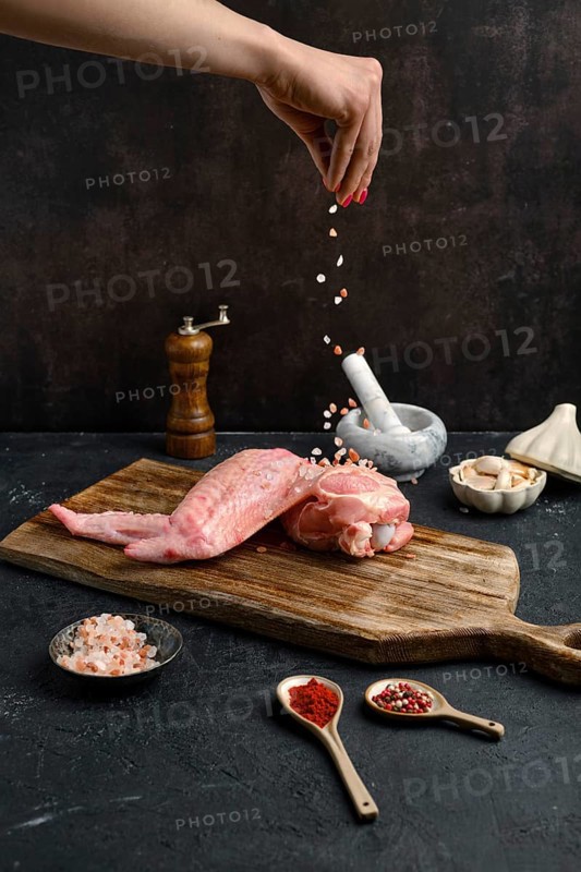 Female hand seasoning with salt raw turkey wing