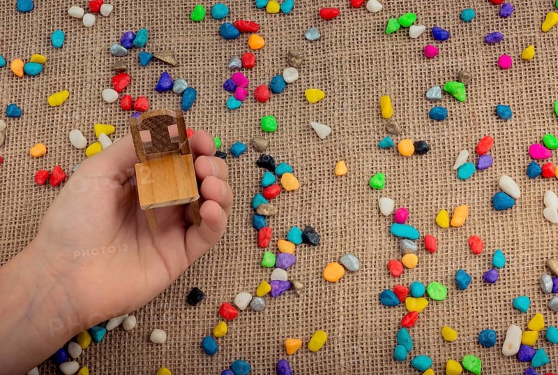 Little chair in hand amid colorful pebbles on canvas