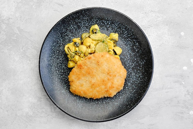Top view of pork schnitzel with potato and pickled cucumber in mustard sauce