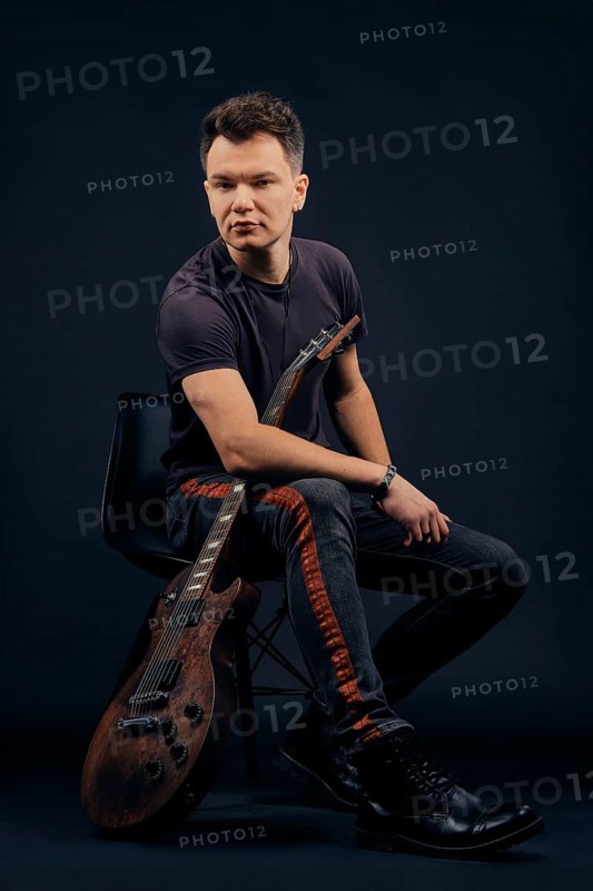 Low key portrait of musician sitting on chair with guitar