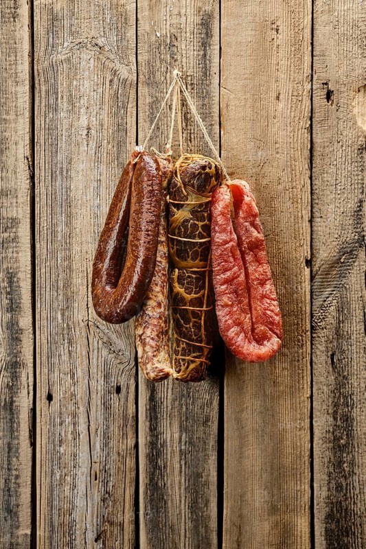 Assortment of dried meat and sausages hanging on a barn wall