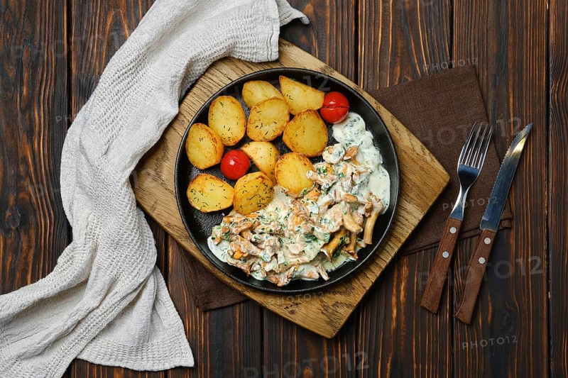 Top view of potato wedges with chanterelles and pork in cast iron skillet
