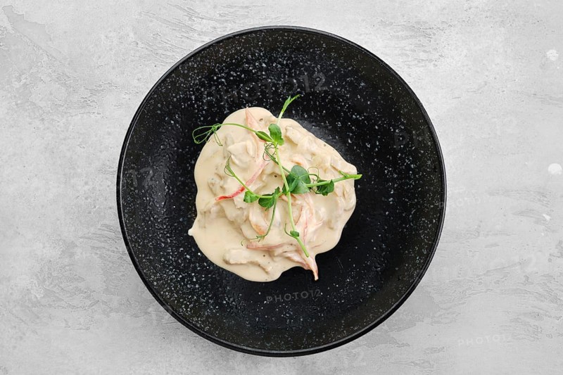 Pieces of chicken meat with bell pepper and creamy white sauce on a plate
