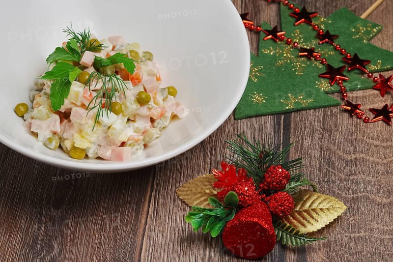Russian traditional salad olivier with pea on wooden table near new years decorations