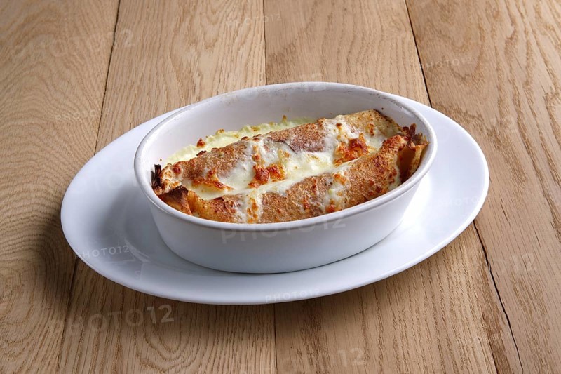 Fried pancakes stuffed with ham and covered with melted cheese on wooden table