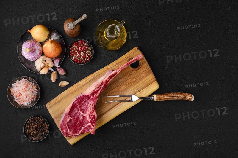 Overhead view of raw beef cowboy steak with spice and seasoning ready for cooking