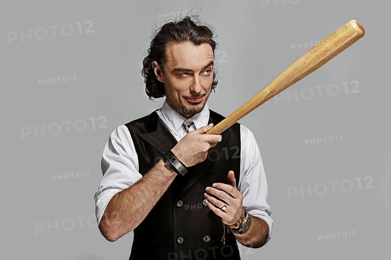 Dramatic man in white shirt and black vest with long curly hair holding baseball bat