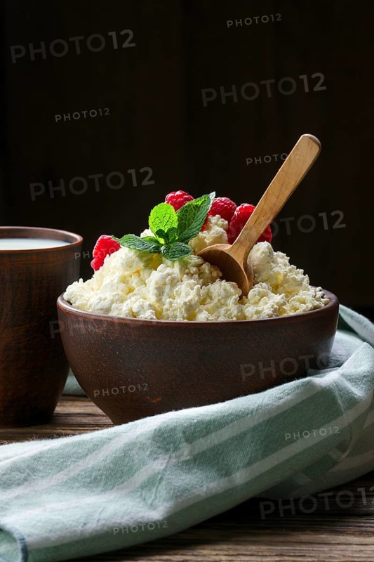 Fresh cottage cheese with raspberries and wooden spoon in clayware on wooden table