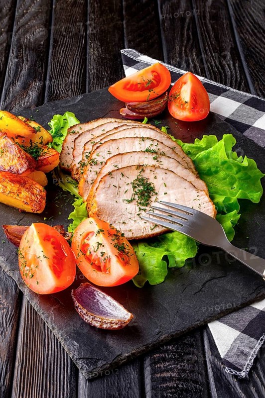 Sliced baked ham with fresh tomatoes on a stone plate in a rustic style