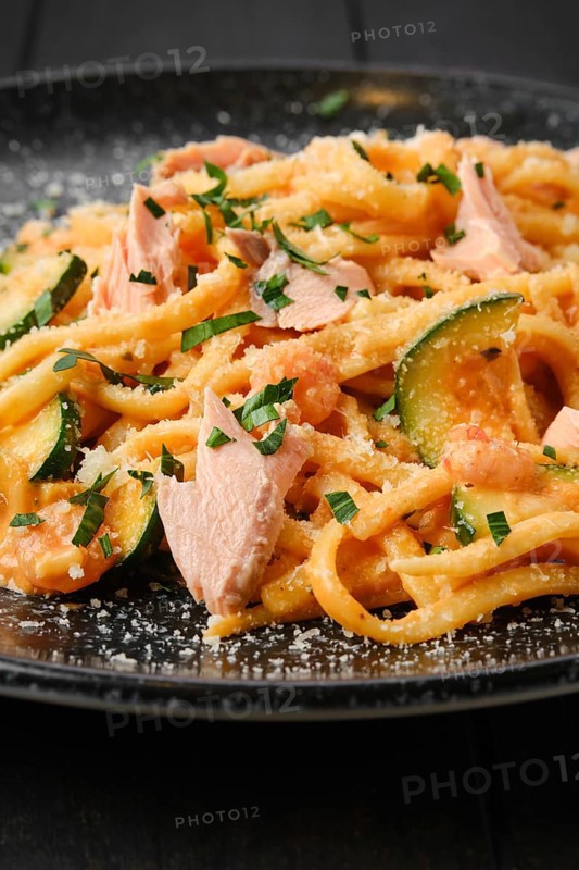 Closeup view of pasta with salmon and zuccini with grated parmesan on a plate