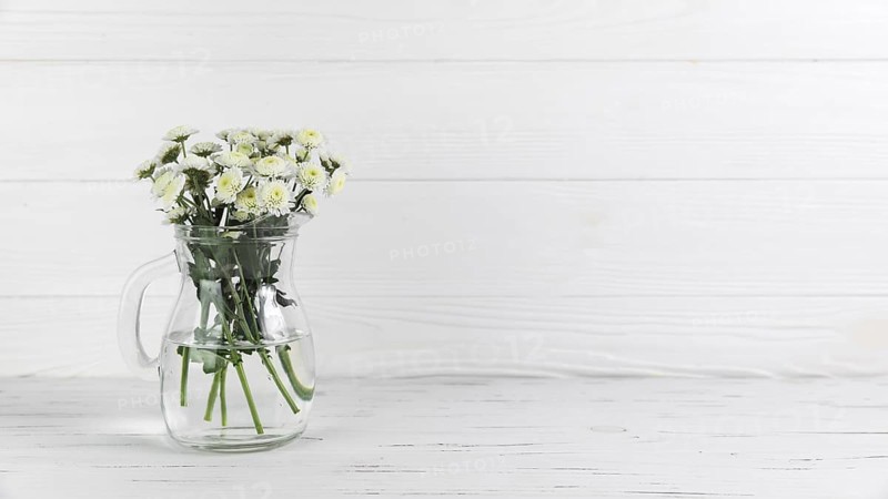 Chrysanthemum flowers inside glass jug against white wooden background