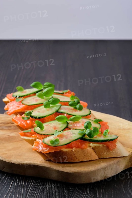 Sandwich with salmon on wooden plate on dark wooden table with copy spase
