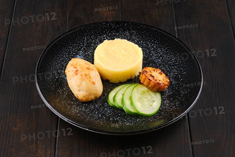 Fried chicken cutlet with mashed potato and slices of fresh cucumber and grilled corn