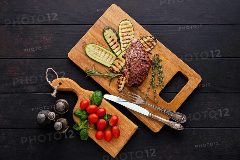 Top view of beef steak and zucchini served with fresh tomato cherry and basil on wooden cutting board
