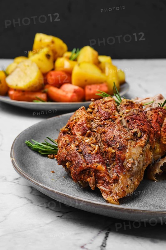 Closeup view of pulled lamb shoulder meat baked in oven with potato and carrot on marble table
