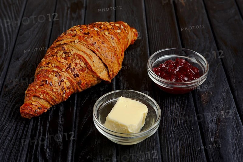 Croissant with jam and butter on dark wooden table