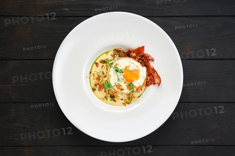 Top view of fried egg with bacon slices and chips served with creamy sauce