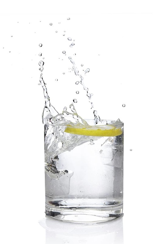 Ice cube and lemon splashing cocktail in oldfashioned glass. Drink with splashing citrus isolated on white