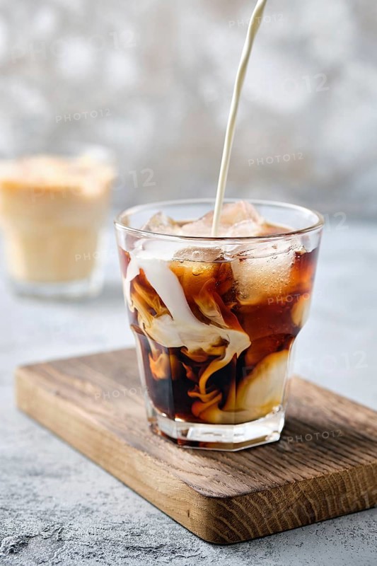 Pouring cream in iced coffee in rocks glass