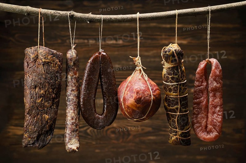 Assortment of dried meat and sausages hanging on a stick in a barn