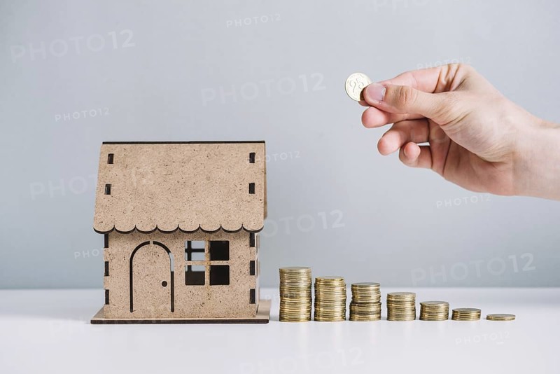 Person s hand stacking coins near house model