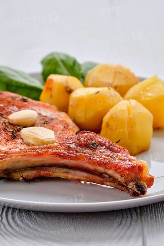 Steak with bone and potato baked in oven in a roasting pan with garlic and thyme