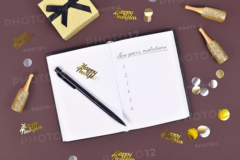 New year's resolutions. Writing a list of plans in open notebook surrounded by New Year party decoration