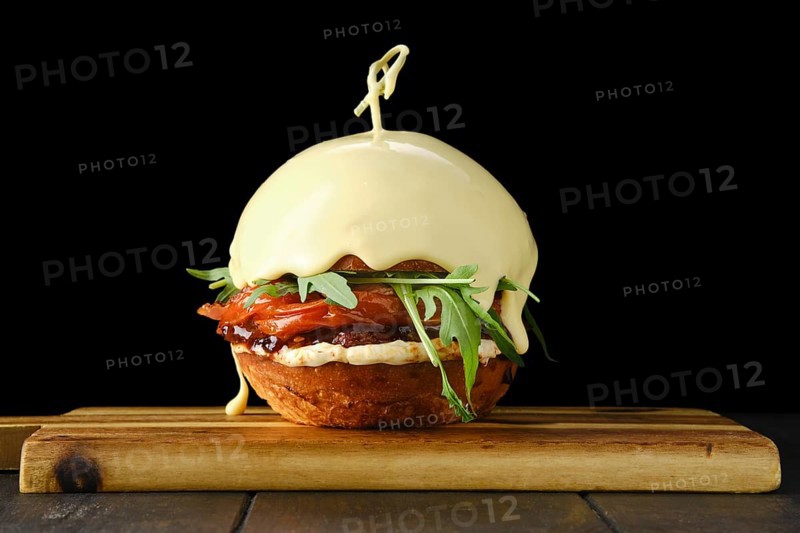 Burger with beef and top bun covered with melting cheese on wooden serving board over black background
