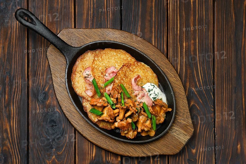 Top view of potato pancakes with chanterelles and pork in cast iron skillet