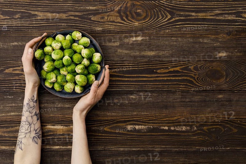 Overhead view of fresh brussel sprout in hands over wooden background