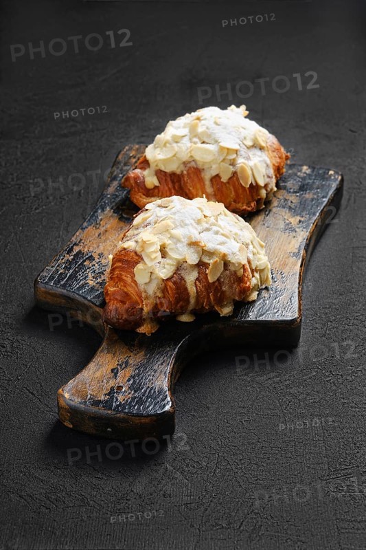 Two crispy croissant with caramel and peanut shavings on wooden serving board